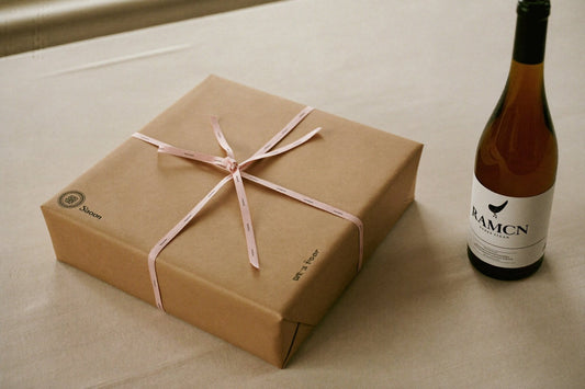Wrapped gift with ribbon beside a bottle of white wine